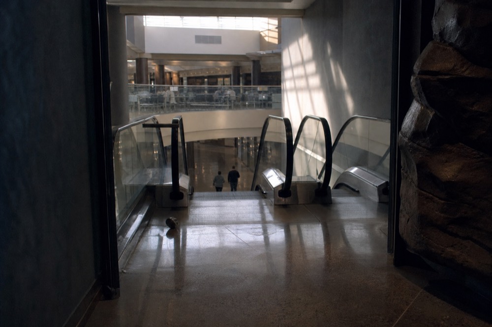 A walkway in a shopping mall basement with a food court entrance and escalators, no text, no logos, no people.