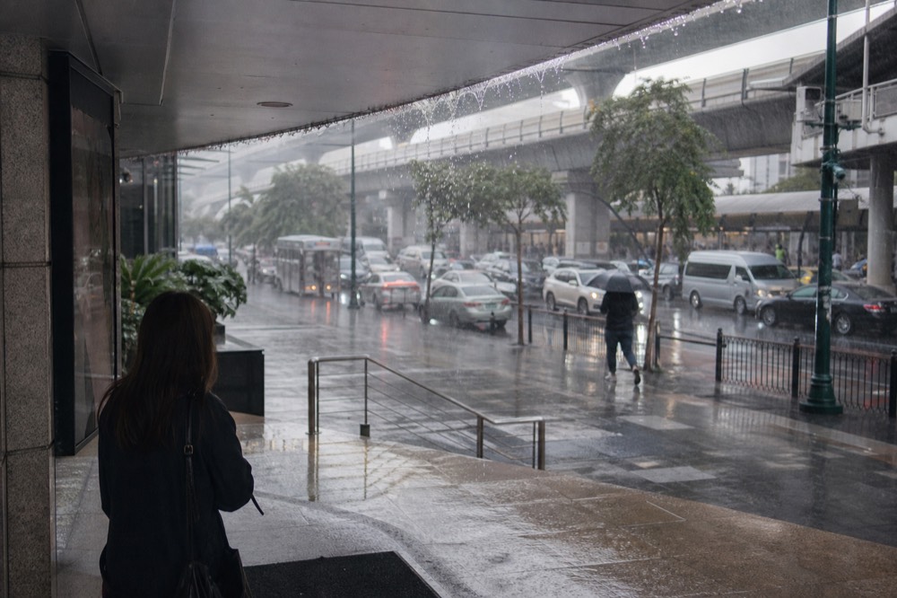 Rain falling on a Bangkok street outside a shopping mall entrance, no text, no logos, no people.
